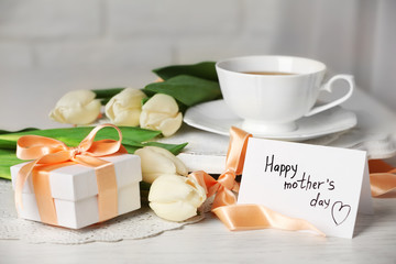 Happy mother day greeting with tulips and cup of tea on wooden table closeup