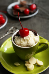 Chocolate cake in a green mug served with two plates of cherries and chocolates, close up