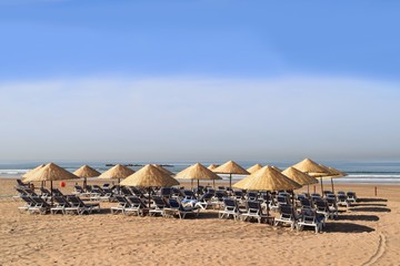 Sonnenliegen und Sonnenschirme warten aufgerreiht am Strand auf Sonnenanbeter