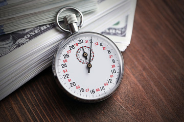 Stopwatch with dollar banknotes on wooden background. Time is money concept