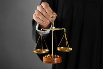 Judge holding scales of justice on grey background