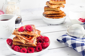 Plate of belgian waffles with fresh berries and fruit syrup on a white kitchen table.