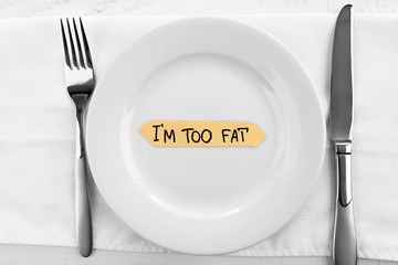 Piece of paper with text I'm TOO FAT in plate on wooden table with knife and fork, top view