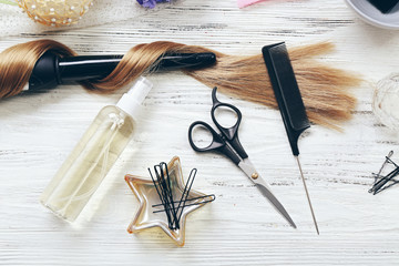 Strand of hair with flowers, barber equipment and tools on light wooden background