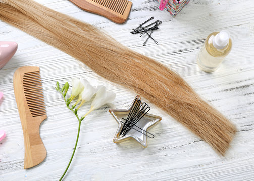 Strand of hair with flowers and barber tools on light wooden background