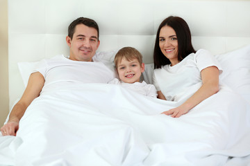 Fototapeta premium Happy family of mother, father and son lying in bed at home