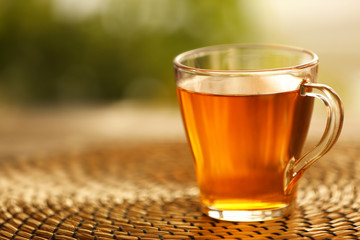 Glass cup of tea on wicker mat against blurred background