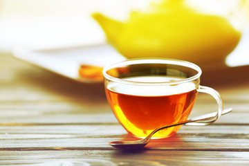 Glass cup of tea with teapot on wooden table against blurred background