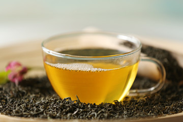 Glass cup of green tea with leaves on wooden plate closeup