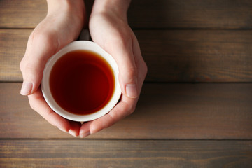 Female hands holding cup of tea on wooden background