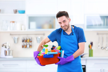 Man holding plastic basin with brushes, gloves and detergents in the kitchen