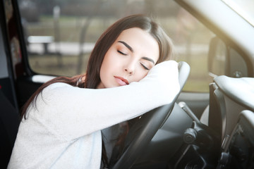 Tired young woman asleep on steering wheel in her car.