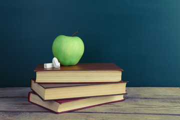 Few books with green apple and chalk on table