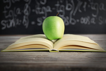 Open book with green apple on table