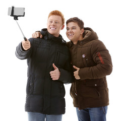 Two teenager boys in winter clothing making photo by their self with mobile phone, isolated on white
