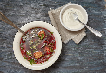 Beetroot soup with beef , vegetables and tomatoes on a wooden table top . Rustic style .