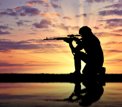 Silhouette of man aiming with rifle during sunset