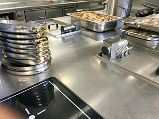 Großküche mit induktionsplatte, gestapelte Pfannen, Fisch und Gemüse auf Gastronorm Bleche 