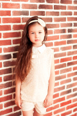 Beautiful baby girl 5-6 year old wearing stylish clothes in room over brick wall. Looking at camera. Childhood.