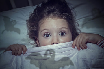 scared cute little girl under the blanket in her bed - obrazy, fototapety, plakaty