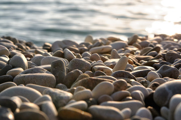 Obraz premium Sea gravel shore or beach with sea water at sunset
