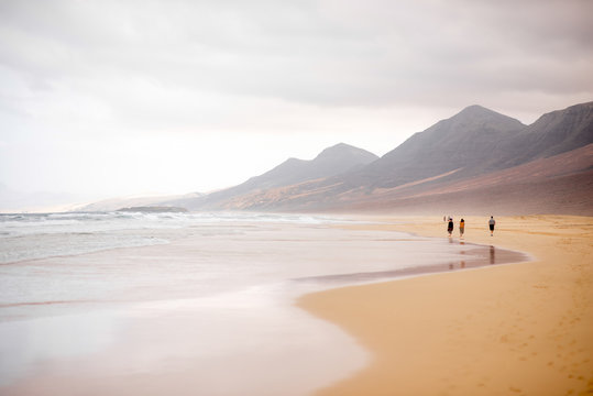 Cofete Beach With People Walking At The Cloudy And Foggy Weather On Fuerteventura Island In Spain