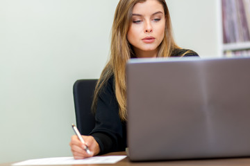 Woman using a laptop computer and writing in her office