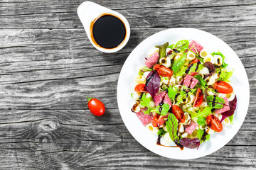 shell pasta delicious salad with mixed lettuce leaves, salami on the white dish with nuts, honey and sesame seeds sauce, closeup