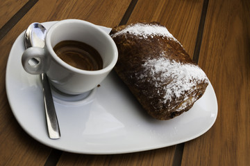 composizione orizzontale fotografica di una tazzina di caffè con una brioche in primo piano per fare colazione