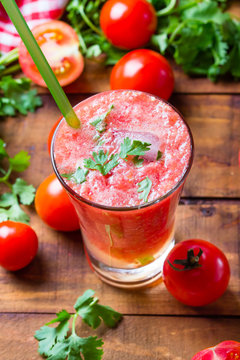 Gass of tomato smoothie, fresh tomatoes and cilantro on a dark wooden background . Vegetarian or healthy eating concept