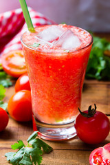 Gass of tomato smoothie, fresh tomatoes and cilantro on a dark wooden background . Vegetarian or healthy eating concept