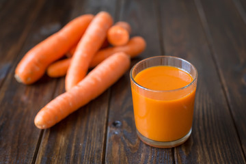 Carrot juice and fresh carrot on a wooden background