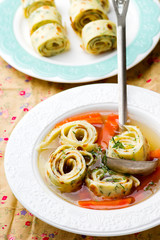 Broth with pancakes and carrots in a white plate.