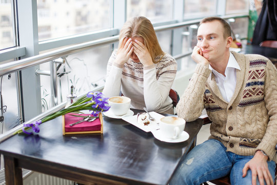 quarrel loving couple in a cafe. after a quarrel. girl sitting at a table covering his face with his hands, sad man looks away