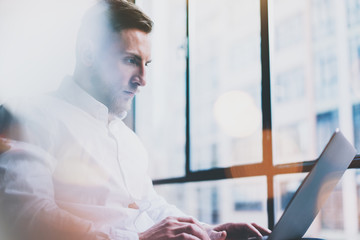 Bearded young businessman working on modern loft office. Man wearing white shirt and using...