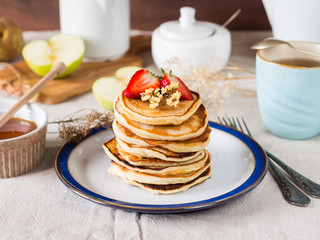 Breakfast with stacked yogurt pancakes with strawberries on beige table cloth