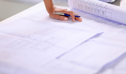 Portrait of female architect with blueprints at desk in office, isolated