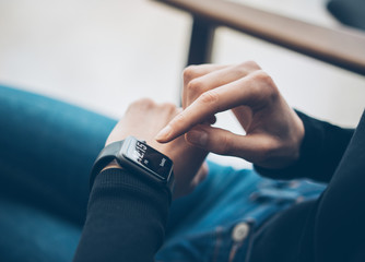 Closeup photo of female hand touching screen generic design smart watch. Film effects, blurred background. Horizontal