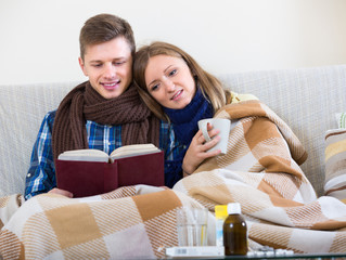 Couple sitting under blanket with book.