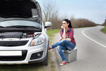 Girl sitting beside car with opened hood