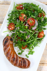 Fried sausage and salad with arugula, tomato and red onion
