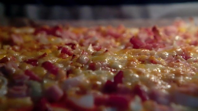 A pizza topped with ham, bacon and cheese, baking in the oven (close-up)