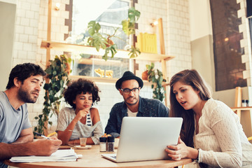 Creative team sitting at cafe and looking at a laptop