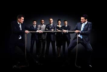 Two business men pulling rope in a competition. in the background is a group of business people