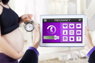 Pregnant mother with pregnancy app and alarm clock
