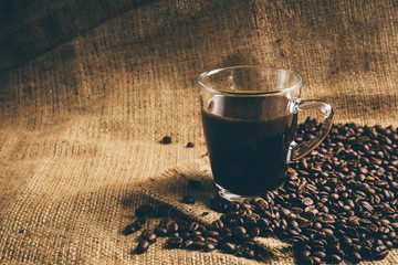 glass cup of espresso coffee with coffee bean on traditional sack textile. Vintage retouching.