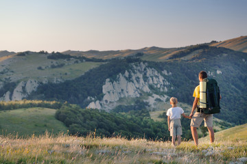 Naklejka na ściany i meble Man and young boy standing in a mountain meadow. 