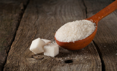 white sugar in wood spoon with sugar cubes closeup