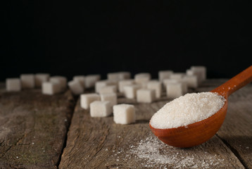 Fototapeta na wymiar white sugar in a wooden spoon and sugar cubes