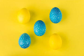 Blue and yellow Easter eggs on bright yellow background, top vie